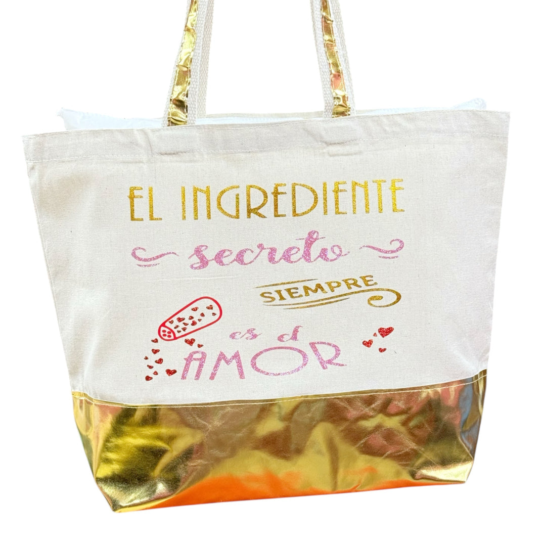 Bolsa tote bag blanca con frase “El ingrediente secreto siempre es el amor” y base dorada, diseño exclusivo de Sfinge